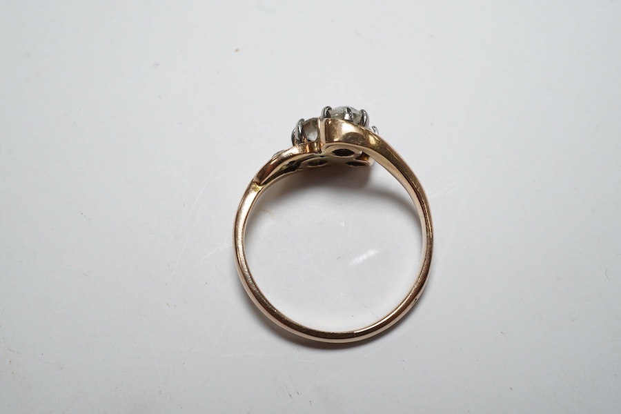 A yellow metal and three stone diamond set crossover ring, with single stone diamond set shoulder, size K, gross weight 2.4 grams. Condition - poor to fair